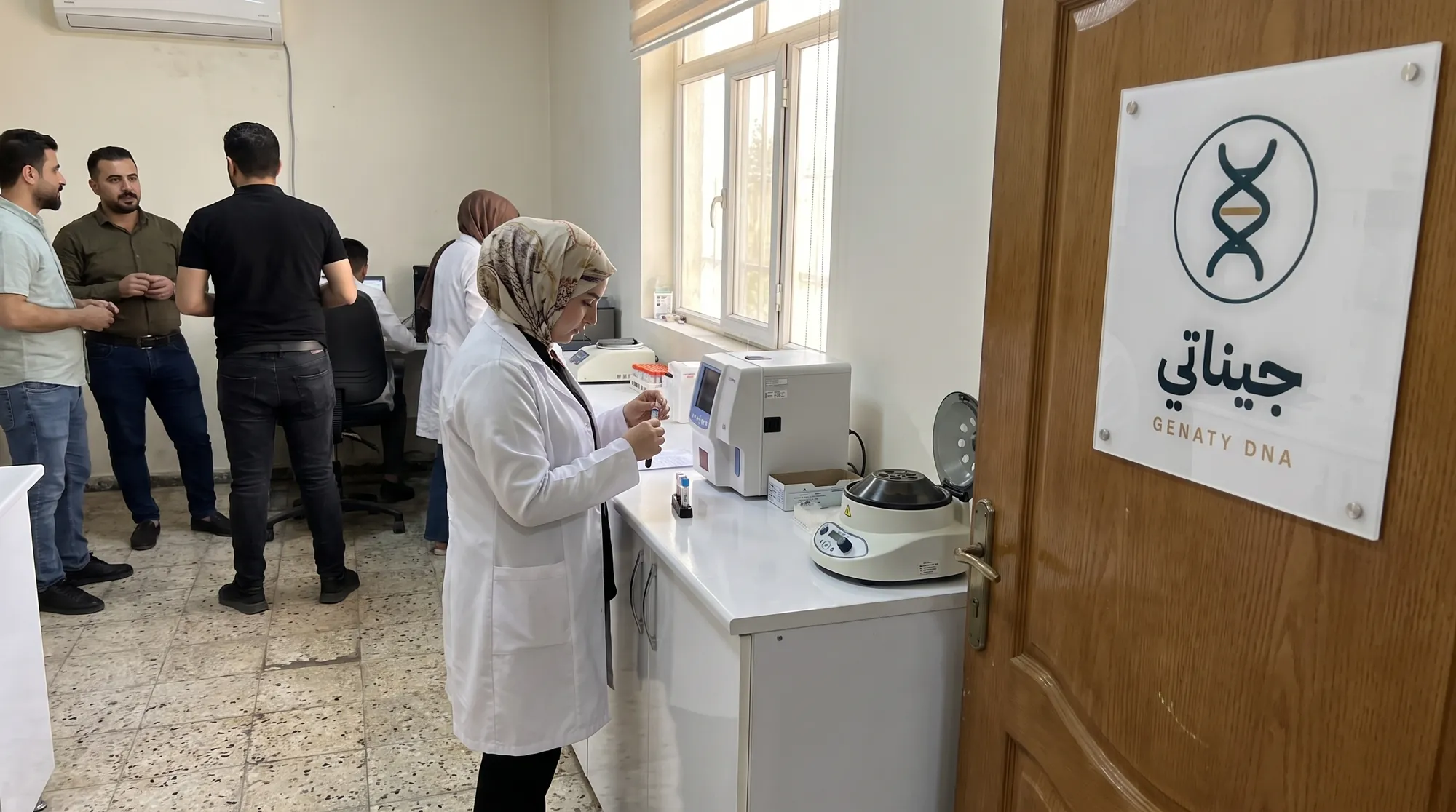 مختبر جيناتي في أربيل: جهاز التحليل وشعار جيناتي على الجدار